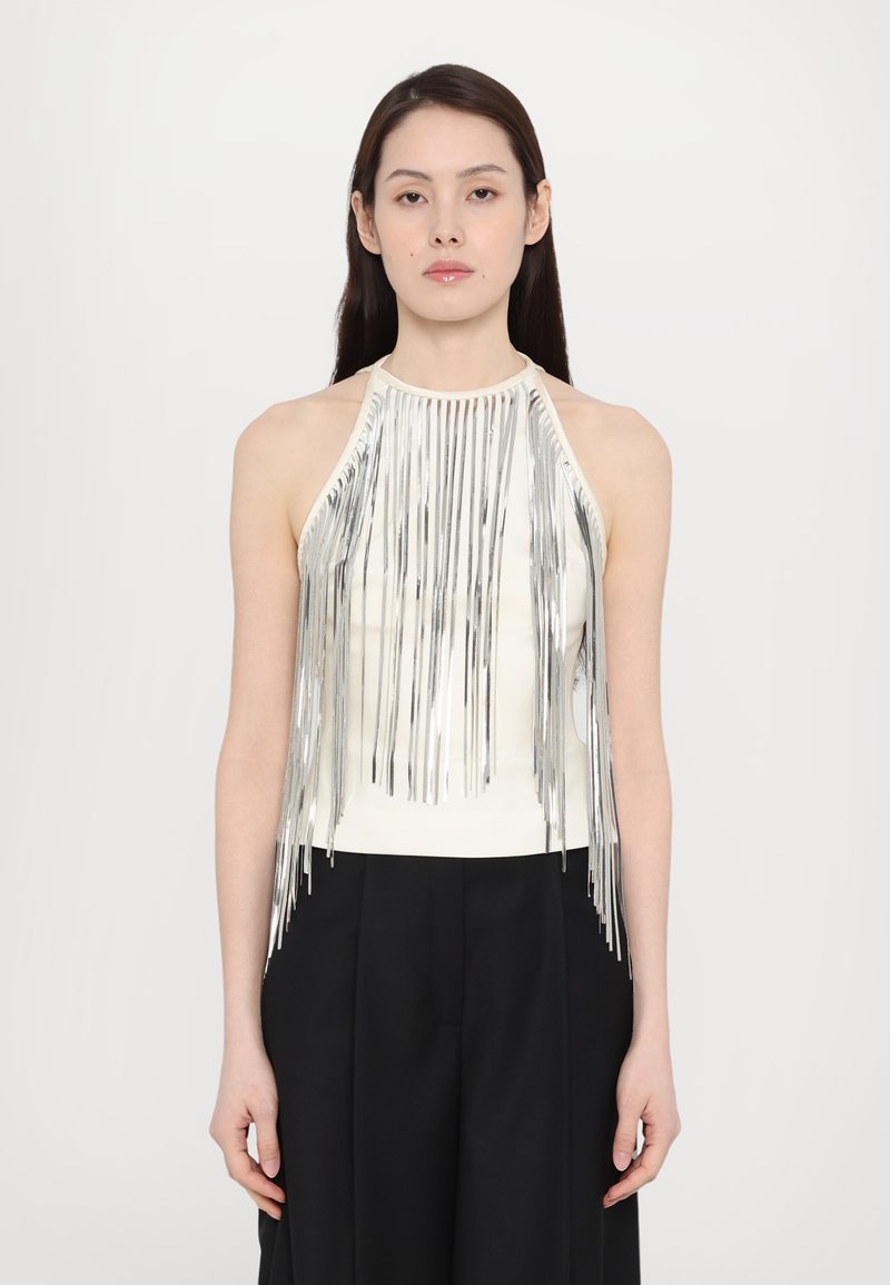 Top halter cu franjuri argintii și un corset alb, având fire metalice care se scurg în jos, asociat cu pantaloni negri, largi.