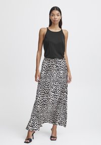 Crna majica na naramenice u paru s dugom bijelom suknjom s više slojeva koja ima odvažan crni leopard uzorak, upotpunjena crnim sandalama na visoku petu.