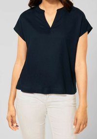 Navy blue lyhythihainen paita, jossa on V-pääntie ja väljä malli, valmistettu pehmeästä kankaasta. Paidassa on kaareva helma ja hienovaraisia ompeluyksityiskohtia.