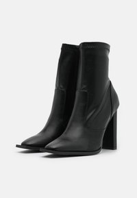 Černé kožené kotníkové boty s špičatou špičkou, hladkým povrchem a robustním vysokým podpatkem. Mají prošívané detaily na svršku.