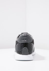 Chaussure de sport noire et grise avec une maille texturée et des accents en cuir lisse, équipée d'une semelle en caoutchouc blanche et d'un logo "new balance" sur le talon.