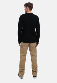 Black textured sweater with ribbed hem, paired with khaki cargo pants featuring side pockets. Model facing away, standing on a plain background.