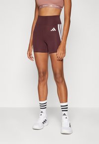 Burgunderfargede treningsshorts med høy livlinje, hvite Adidas-striper på sidene, kombinert med hvite sokker med svarte striper og sneakers med svarte detaljer.