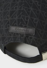 Casquette noire avec un tissu à texture imprimée et un logo en cuir Calvin Klein en relief à l'arrière, mettant en avant un design épuré.