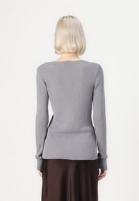 Gray ribbed long-sleeve top with a round neckline, fitted silhouette, and soft texture, paired with a dark brown satin skirt.
