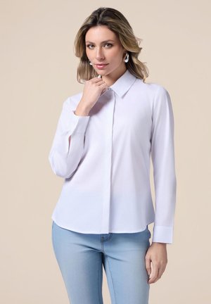 Witte lange mouwen shirt met een puntige kraag, gemaakt van een soepele stof, met een knoopsluiting aan de voorkant en een licht gebogen zoom. Gedeeltelijk gedragen met lichtblauwe jeans.