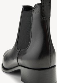 Botte Chelsea en cuir noir avec panneau élastique sur le côté, bout rond et un talon bloque solide. Texture lisse et détails de couture subtils.