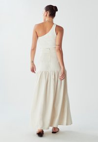 Biała, prążkowana bluzka na jedno ramię połączona z beżową, warstwową spódnicą maxi. Strój charakteryzuje się dopasowaną talią oraz zwiewnym, teksturowanym materiałem.