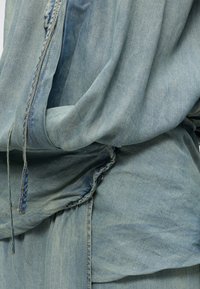 Χαλαρό ανοιχτό μπλε ντένιμ ύφασμα με ορατές ραφές, πτυχώσεις και κορδόνια σε στυλ casual ένδυσης.