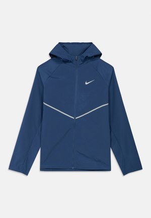Sininen hupullinen kevyt takki, jossa koko etuosan vetoketju, heijastava kalanruotokuvio rinnan poikki ja pieni Nike-logo vasemmalla rinnassa.