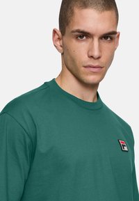 T-shirt in cotone verde con scollo rotondo e logo Fila ricamato sul lato sinistro del petto. Design semplice con maniche corte.