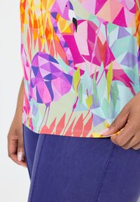 Barevná košile s geometrickými vzory plameňáků a listí v odstínech růžové, fialové a zelené. Krátké rukávy, měkká tkanina, živý design.