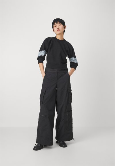 Felpa nera con strisce grigie texturate, pantaloni cargo neri a gamba larga con tasche e cerniere, abbinati a stivali neri alla caviglia.