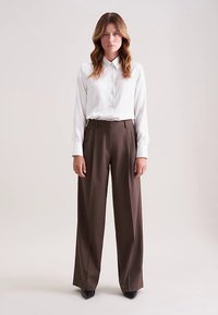 Koszula w białe paski zapinana na guziki, zestawiona z brązowymi spodniami o wysokim stanach i szerokich nogawkach. Gładki materiał o dopasowanym kroju i subtelnym połysku.