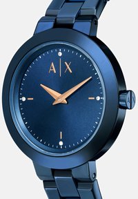 Krožno nerjaveče jeklo uro z modrim kovinskim trakom in številčnico, ki ima rožnato zlate kazalce, diamantne oznake in logotip na 12. uri.