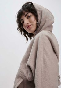 Lichtgrijze fleece hoodie met een ontspannen pasvorm, voorzien van een trekkoord bij de capuchon en zichtbare stikdetails. Zachte textuur, casual ontwerp.