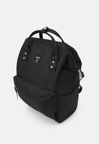 Czarny plecak z nylonu z dwoma górnymi uchwytami, przednią kieszenią na zamek błyskawiczny oraz prostokątnym kształtem. Wyposażony w srebrne akcesoria i etykietę z logo.