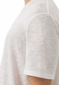T-shirt bianco a maniche corte con una texture sottile, scollo rotondo e un piccolo logo ricamato sulla manica.