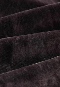 Purpura korduroja audums ar izteikti vertikālām svītrām, kam piemīt maiga tekstūra un neliela spīduma, salocīts pārklājošos slāņos.