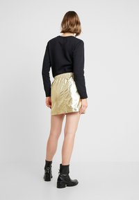 Felicetto cropped nero, gonna mini dorata lucida con vita elastica, abbinata a stivaletti neri alla caviglia. Texture liscia, finitura metallica.