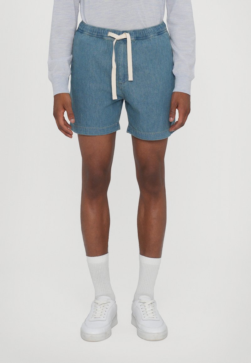 Shorts en denim avec une taille élastique et un cordon de serrage crème, de couleur bleu clair, avec des ourlets retroussés et une coupe décontractée.