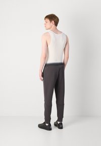 Grå tapered joggere med lommer og ribbede manchetter, parret med en hvid tanktop. Båret med sorte sneakers, hvilket viser et sporty look.
