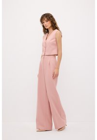 Roze cropped vest met knopen aan de voorkant, gecombineerd met hoogwater, wijde roze broek, beide gemaakt van een gladde stof.