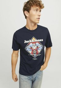 Námořnické tričko vyrobené z bavlny, s grafikou kostlivce Santy na motorce, s bílým textem "Jack&Jones" a barevnými akcenty hor.