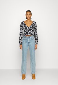 Top longo preto com flores, de mangas longas e decote em V, combinado com jeans de perna reta azul claro e botas de tornozelo bege. Design simples e moderno.