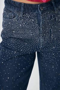 Tamsiai mėlyni džinsai iš džinso audinio, papuošti sidabriniais kalnų krištolo akmenėliais išsibarsčiusiu raštu. Turi klasikinius penkių kišenių dizainą ir metalinį mygtuką užsegimui.