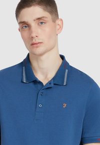 Blauwe polo shirt van een katoenmix, met een contrasterende gestreepte kraag, geborduurd logo op de borst en knoopsluiting.