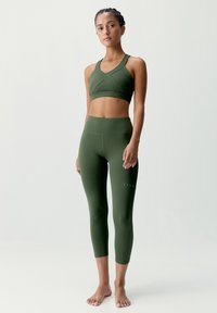 Zelený športový set obsahujúci skrátený športový podprsenka s ostrým dizajnom a legíny s vysokým pásom. Textúrovaná, elastická tkanina, priliehavý strih.