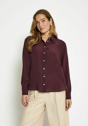 Burgundy long-sleeve blouse with a button-up front, classic collar, and subtle sheen, paired with beige high-waisted pants.