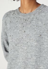 Grå, strikket genser med rund hals, dekorert med spredte sølvperler og en myk, teksturert overflate.