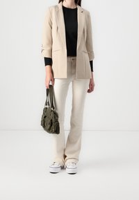 Béžové sako, černý top, světlé béžové džíny, bílé tenisky a tmavě zelená kabelka. Sako má vyhrnuté rukávy; kabelka má několik kapes.