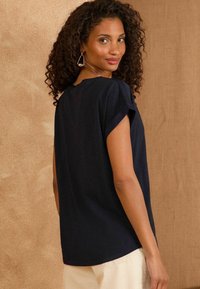 Top navy blue a maniche corte con vestibilità rilassata, realizzato in tessuto morbido, con scollo rotondo e lievi arricciature sulle cuciture delle spalle.