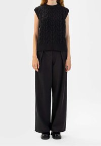 Haut sans manches noir en maille avec motif texturé en forme de vagues, associé à un pantalon noir taille haute à jambes larges et des chaussures noires épaisses.