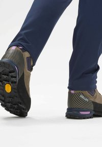 Chaussure de randonnée marron et noire avec une tige en suede texturée, semelle en caoutchouc et accents violets. Caractéristiques d'une semelle Vibram pour une meilleure traction.