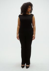 Must kärbitud pluus laia kaelusega, sobitatud mustade kohandatud pükstega. Jalatsid on läikivad mustad kontsakingad. Silmapaistev, veniv kangas.