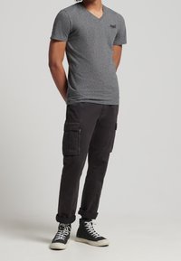 T-shirt grigio a scollo a V con maniche corte, abbinato a pantaloni cargo neri con molte tasche e risvolti. Sneakers alte nere.