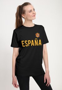 Zwart t-shirt met het woord "ESPAÑA" in vet gele letters en een klein nationaal wapen op de linkerborst.