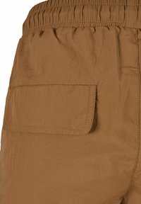 Bruine shorts met een elastische tailleband en een enkele opgestikte zak op de achterkant, gekenmerkt door een textuurstof en contrasterende stikseldetails.