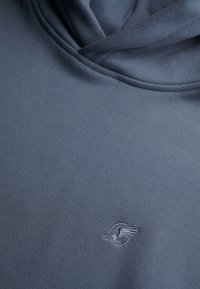 Felpa con cappuccio di colore blu scuro, realizzata in tessuto morbido. Presenta un logo ricamato discreto sul petto. Texture liscia con una vestibilità rilassata.