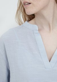 Ljusblå linne-topp med V-hals och en något texturerad yta, med en minimalistisk design och avslappnad passform.