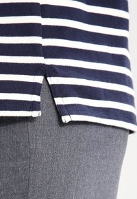 Námořnický a bílý pruhovaný pletený top s zaobleným rozparkem. V kombinaci se šedým materiálem, který ukazuje strukturu a detaily švu.