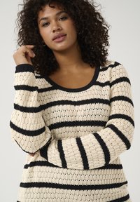 Striped sweater featuring a cream background with black stripes, knitted texture, round neck, and long sleeves.
