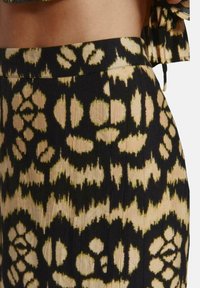 Tela negra y beige con patrones y motivos florales y pliegues verticales. La cinturilla es suave; el material parece ligero y texturizado.