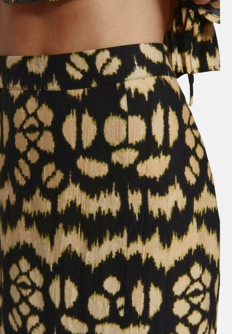 Tela negra y beige con patrones y motivos florales y pliegues verticales. La cinturilla es suave; el material parece ligero y texturizado.