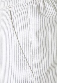 Vitt tyg med blå vertikala ränder, med en sidoficka och texturerad sömnad. Sammanlagt slät yta och lätt material.