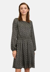 Schwarzes Langarmkleid mit weißem geometrischem Muster, geraffter Taille und A-Linie, aus leichtem Stoff gefertigt.